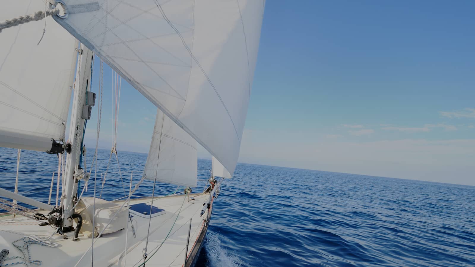 White sailboat with billowing sails gliding across calm blue ocean waters under clear sky