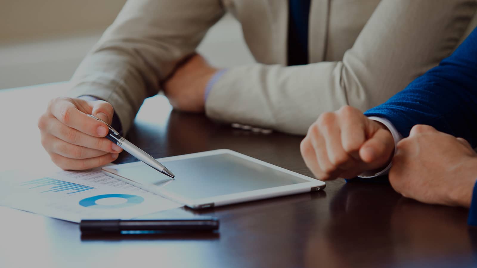 Close-up of hands reviewing printed business documents and charts on a tablet