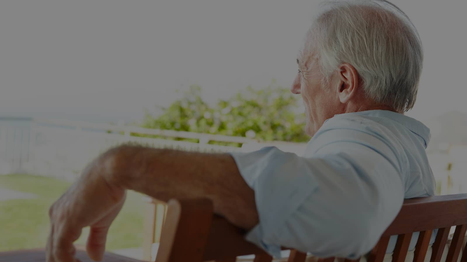 Older man in blue shirt sitting outdoors on wooden bench looking away Older man in blue shirt sitting outdoors on wooden bench looking away