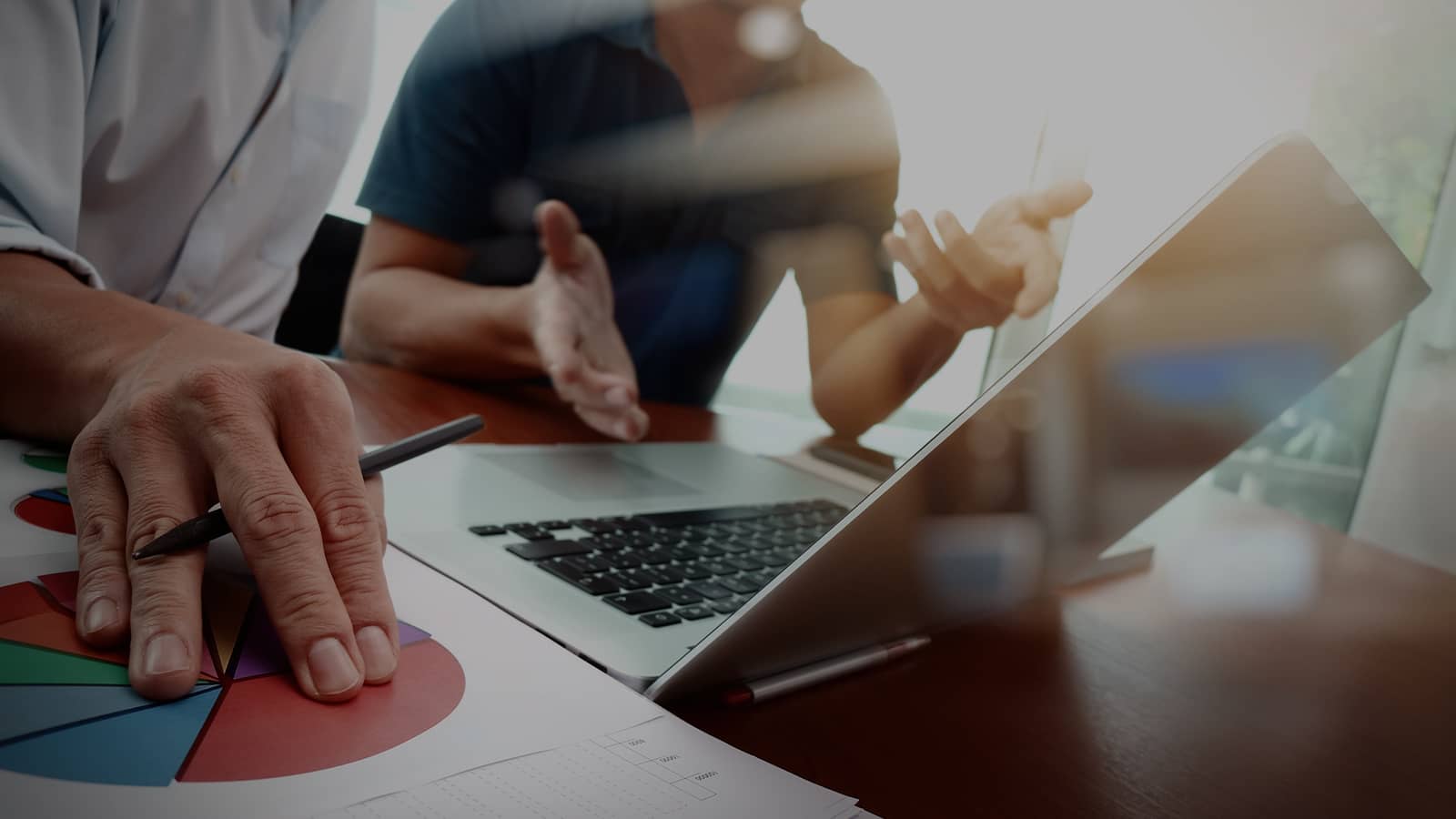 Hands pointing at laptop and colorful pie charts during business collaboration